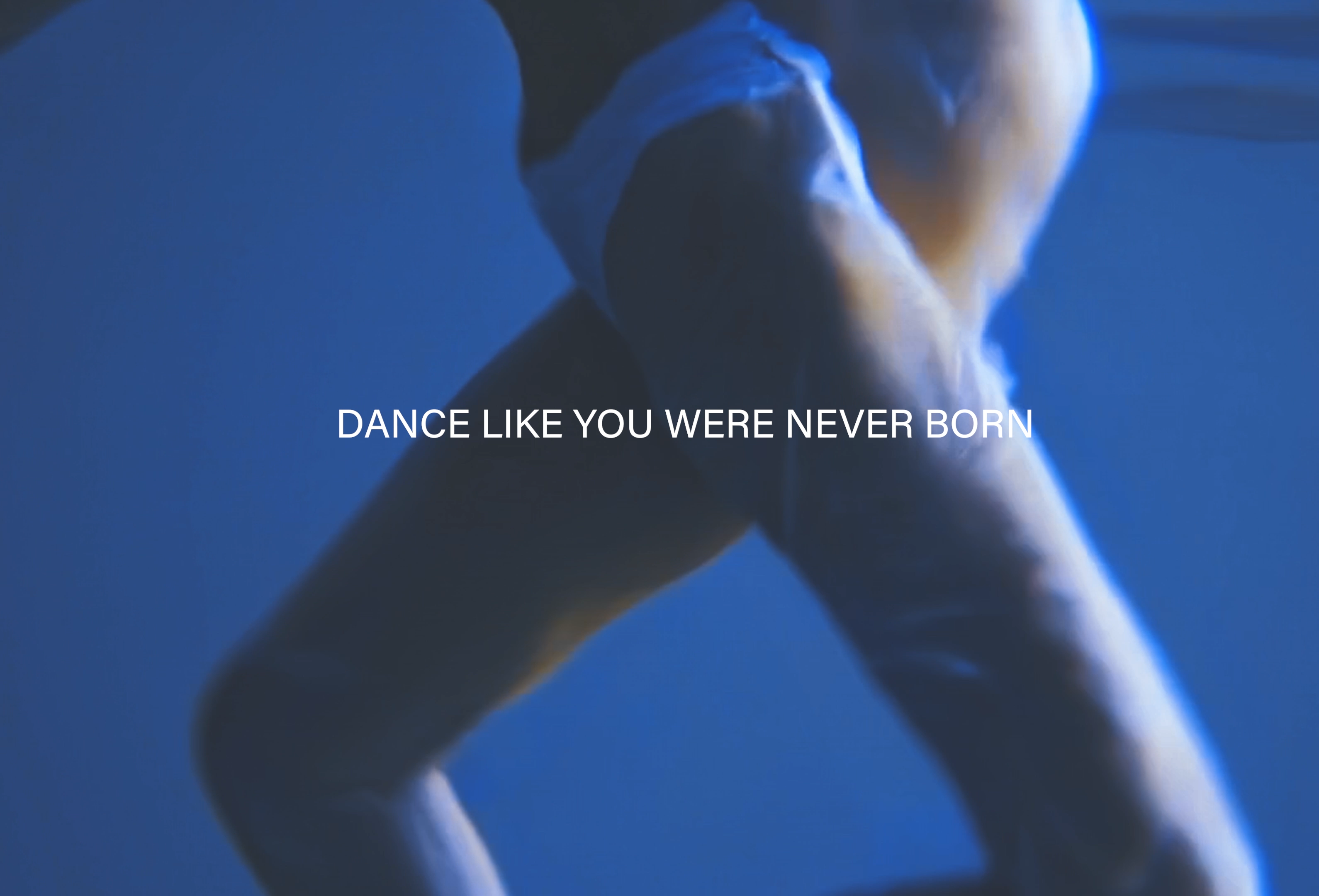 Rough shape of legs against a backdrop of blue water with "Dance Like You Were Never Born" written on the screen in all caps.