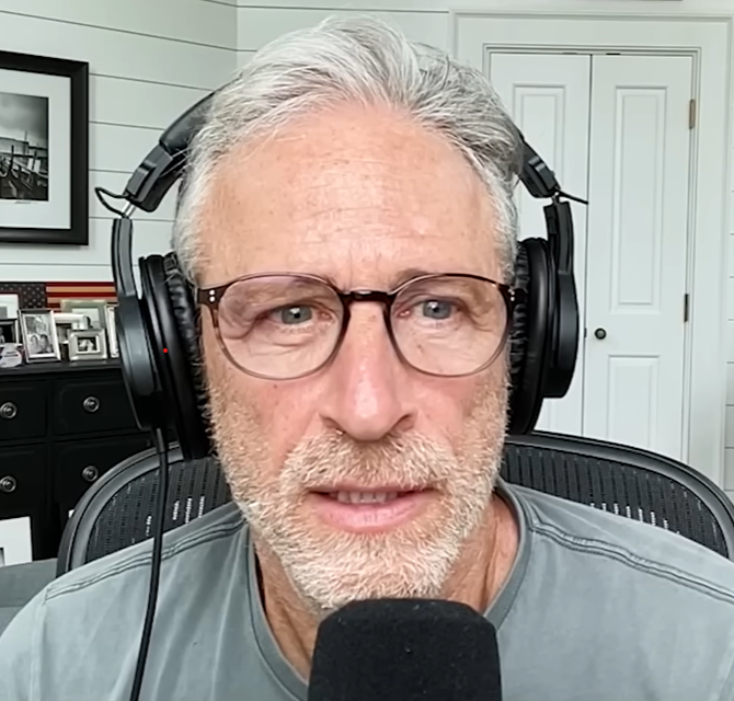 A clearly confused male podcast host with gray hair and beard and light brown glasses.