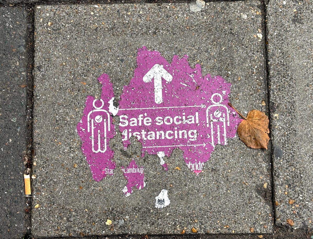A worn purple street decal on a sidewalk warning of "safe social distancing."